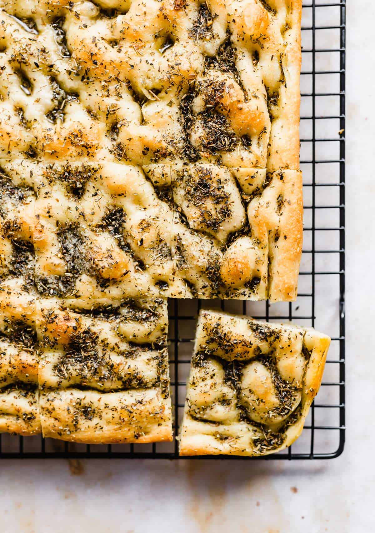 The best Focaccia Bread topped with herb oil on a black cooling rack.