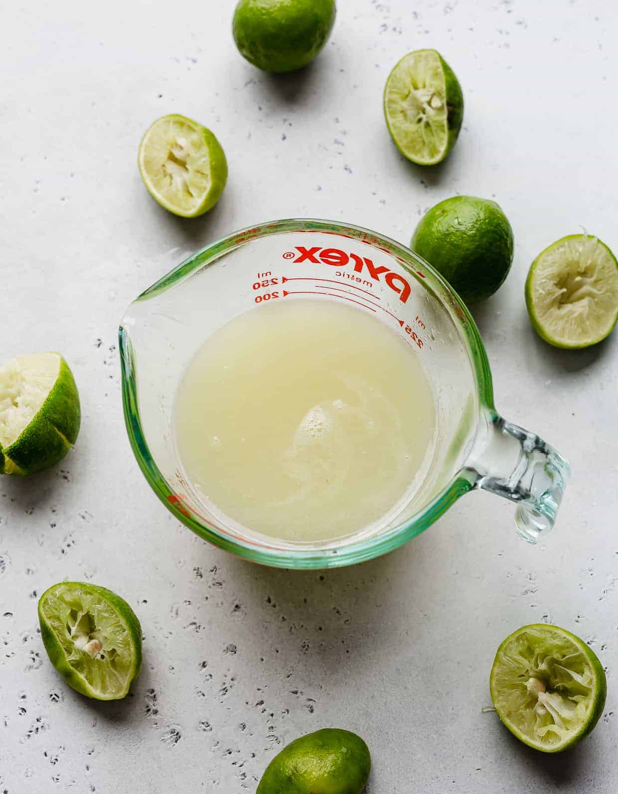 A glass measuring cup full of lime juice, surrounded by key limes.