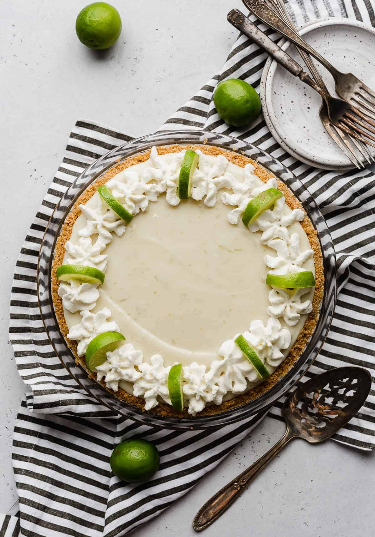 Overheard photo of a key lime pie topped with whipped cream along the edges and lime wedges.