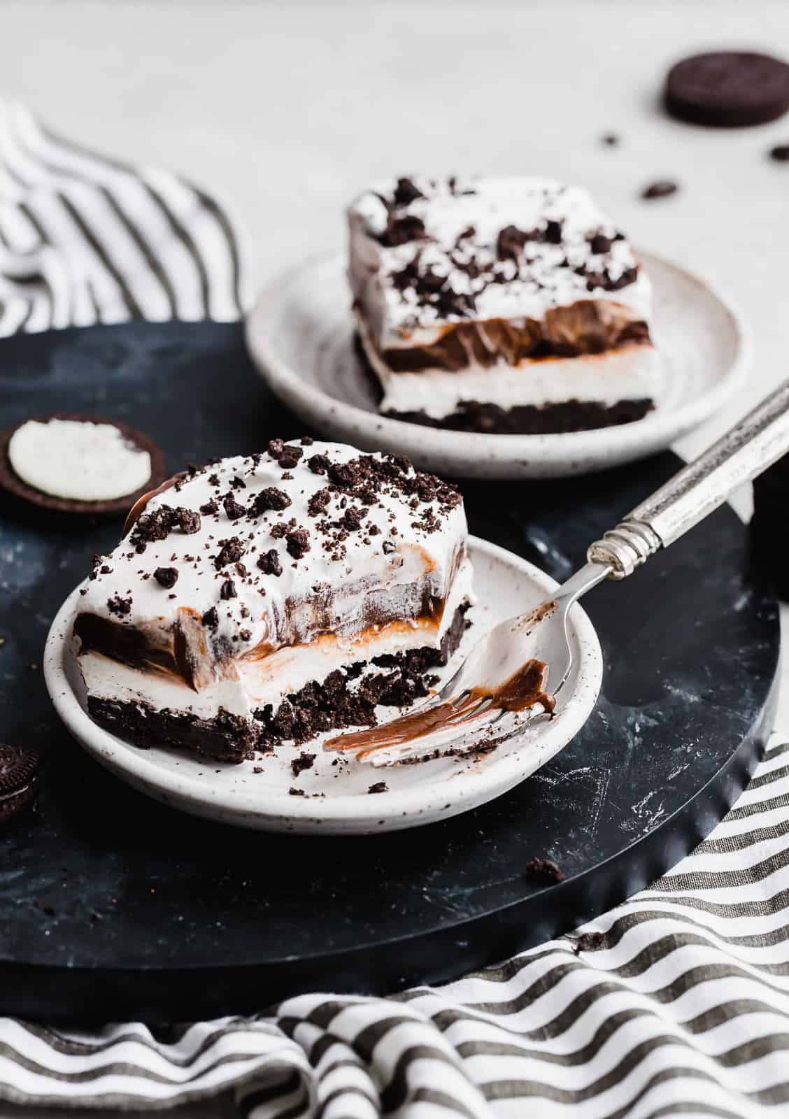 A square slice of Oreo Dessert and fork on a white plate.