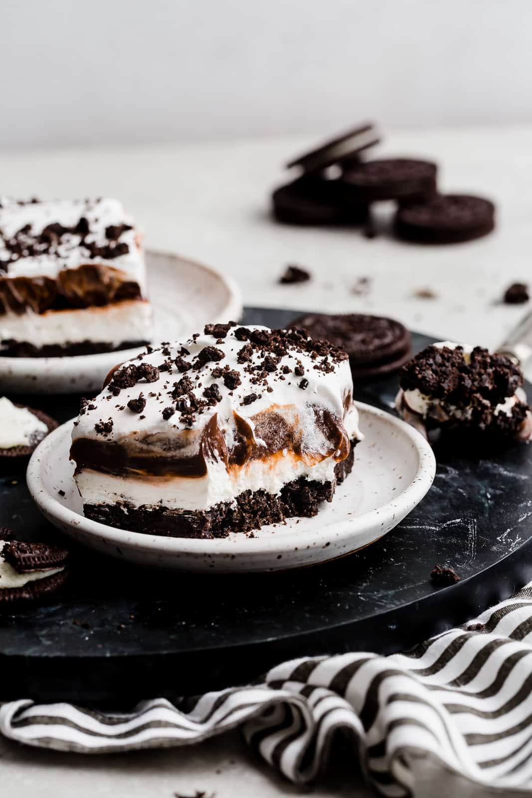 A oreo dessert on a white plate: Oreo crust, cream cheese filling, chocolate pudding, and whipped topping. 