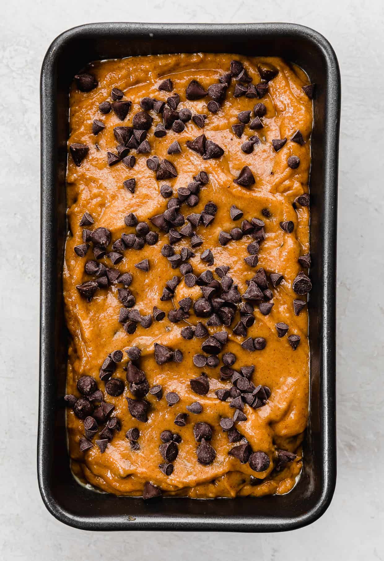 Unbaked Pumpkin Chocolate Chip Bread in a loaf pan topped with mini chocolate chips and semi-sweet chocolate chips.