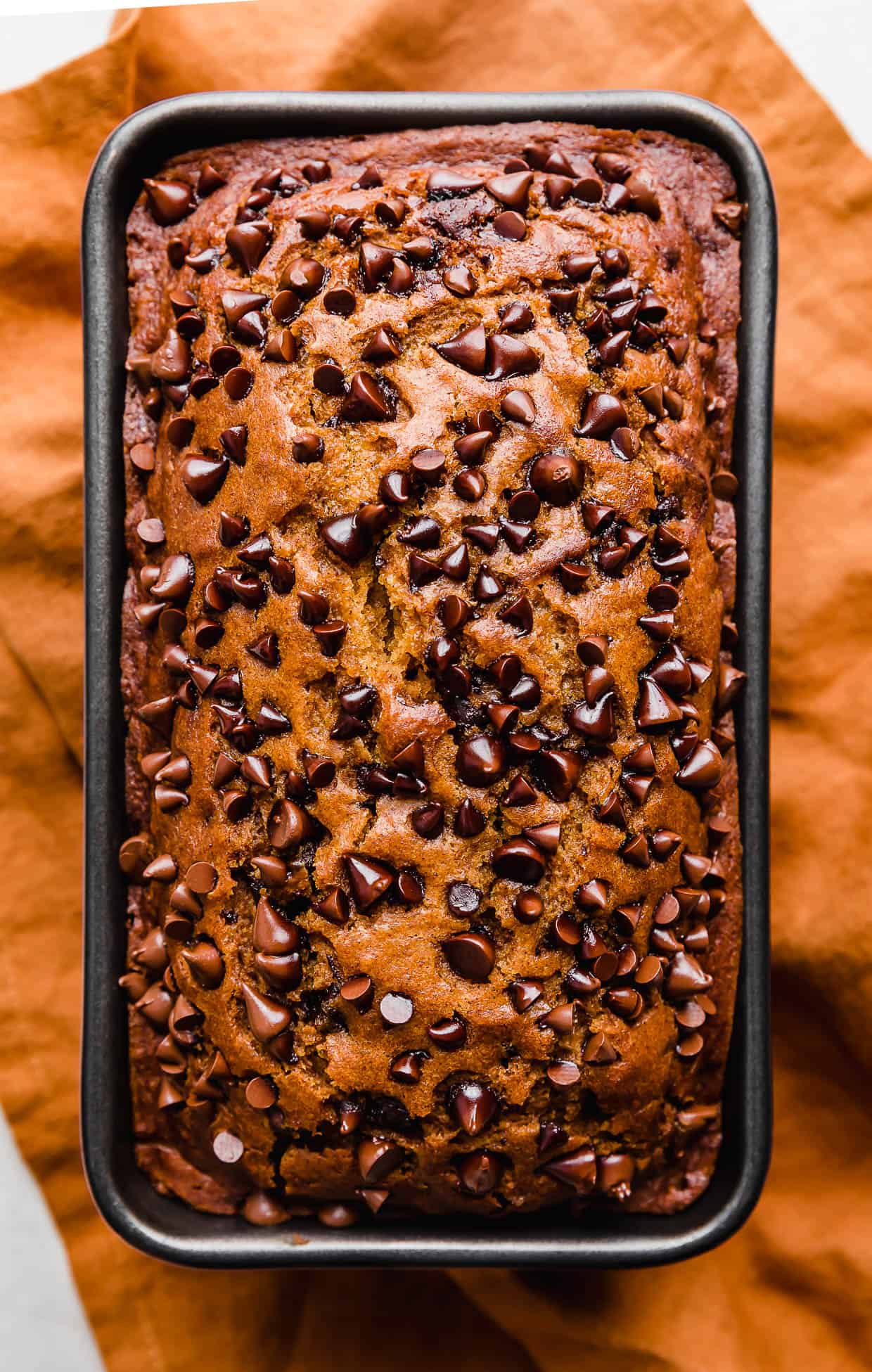 Baked Pumpkin Chocolate Chip Bread in a loaf pan on a burnt orange napkin.