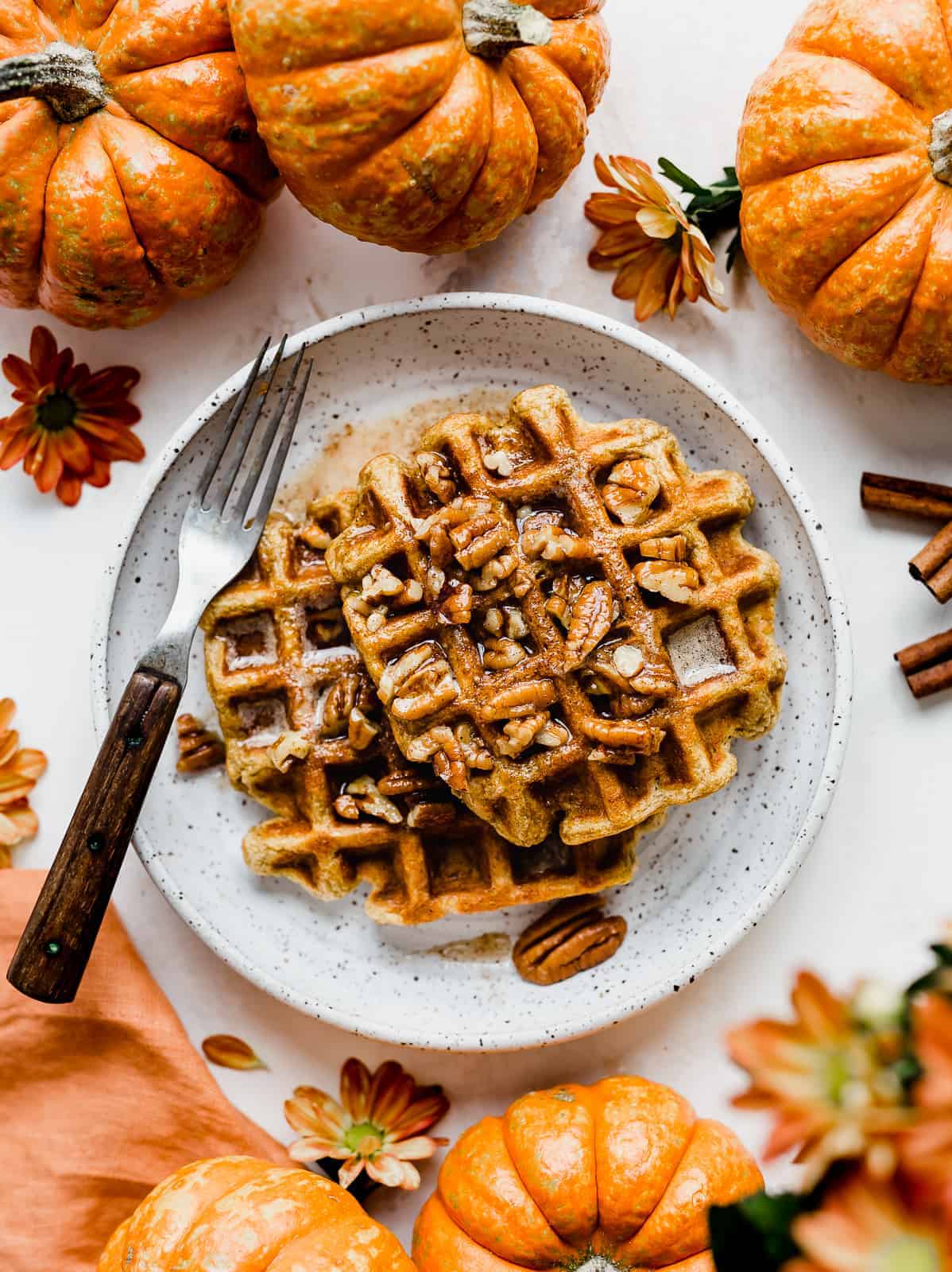Two Pumpkin Waffles on a white plate surrounded by mini pumpkins.