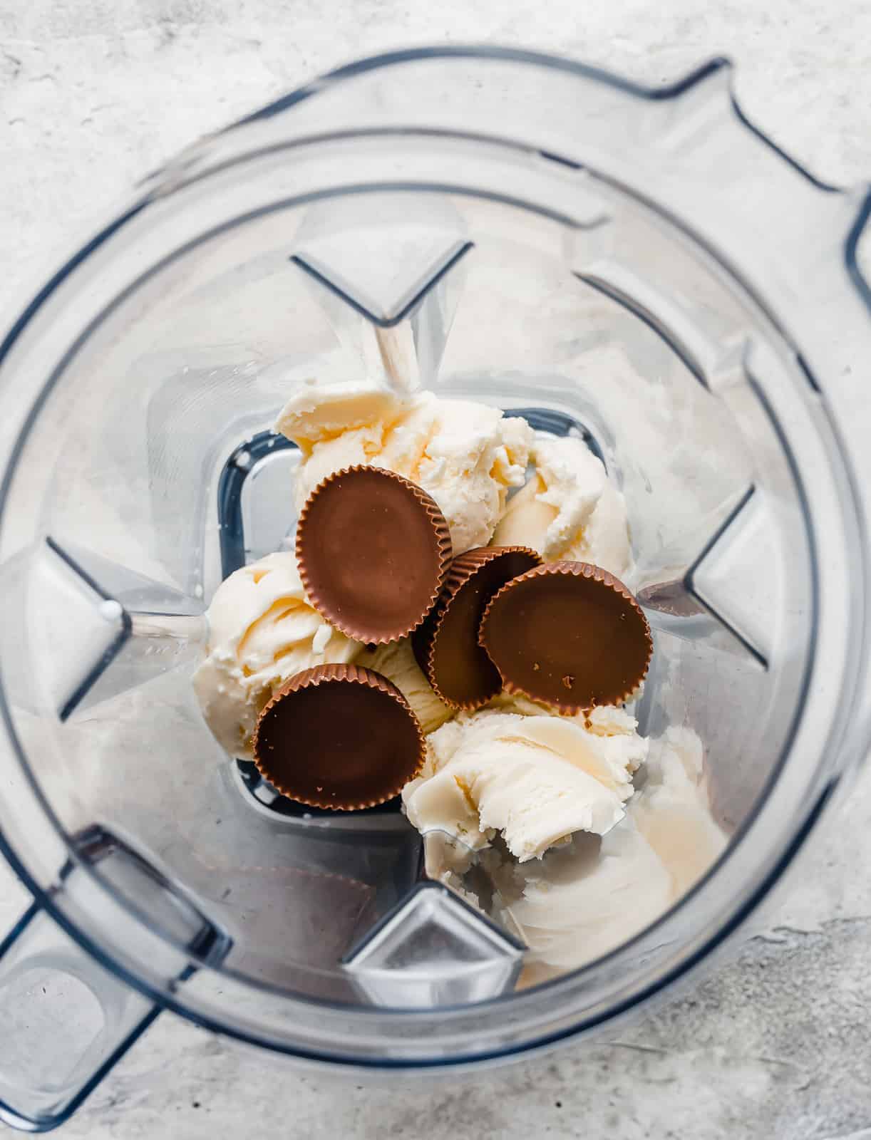 A blender with vanilla ice cream and 4 Reese's peanut butter cups in it.