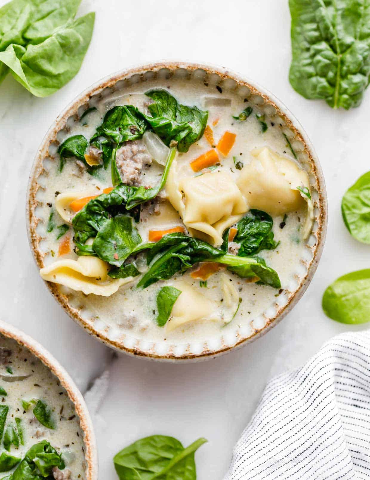 A bowl filled with Sausage Tortellini Soup on a white background.