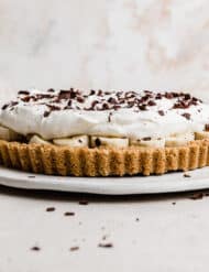 A Banoffee Pie on a white plate, topped with whipped cream and chocolate shavings.