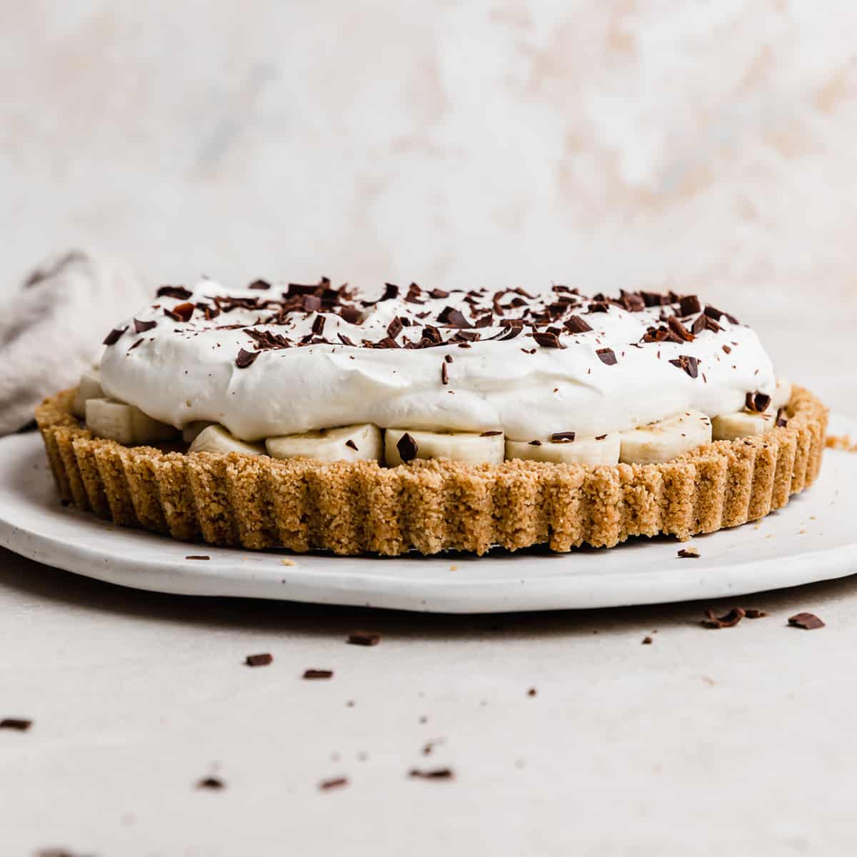 A Banoffee Pie on a white plate, topped with whipped cream and chocolate shavings.