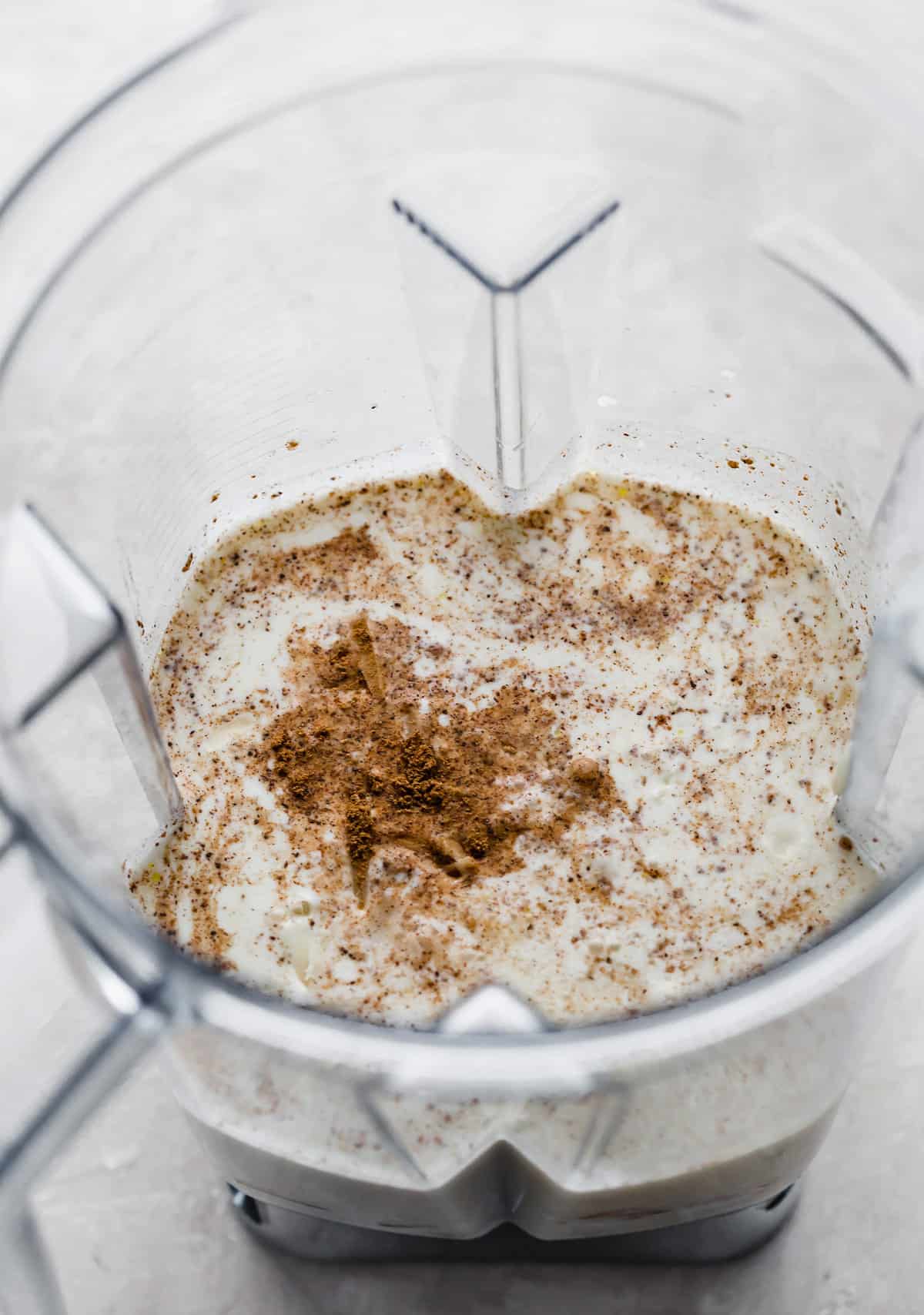 A blender half full of half and half with nutmeg sprinkled overtop.