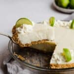 A slice of Key Lime Pie with sour cream on a graham cracker crust balancing on a serving knife.