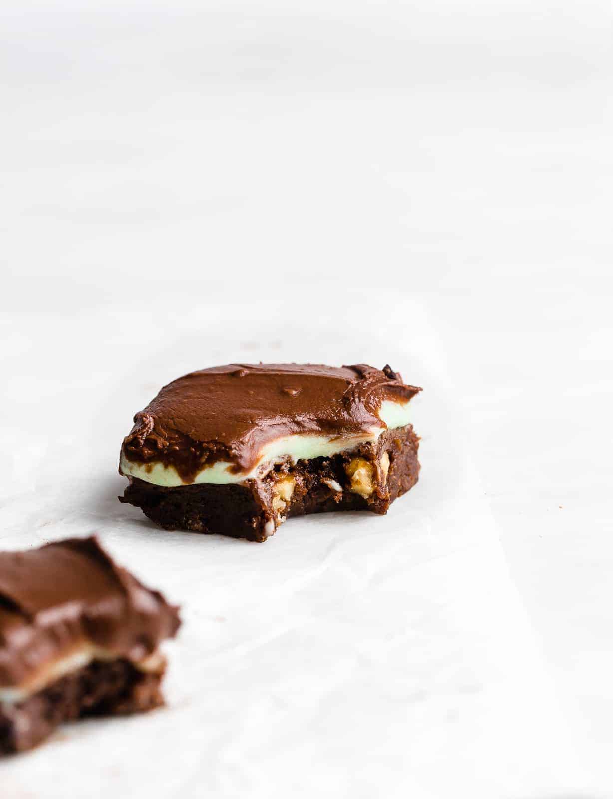 A mint and chocolate frosting covered brownie on a white background.