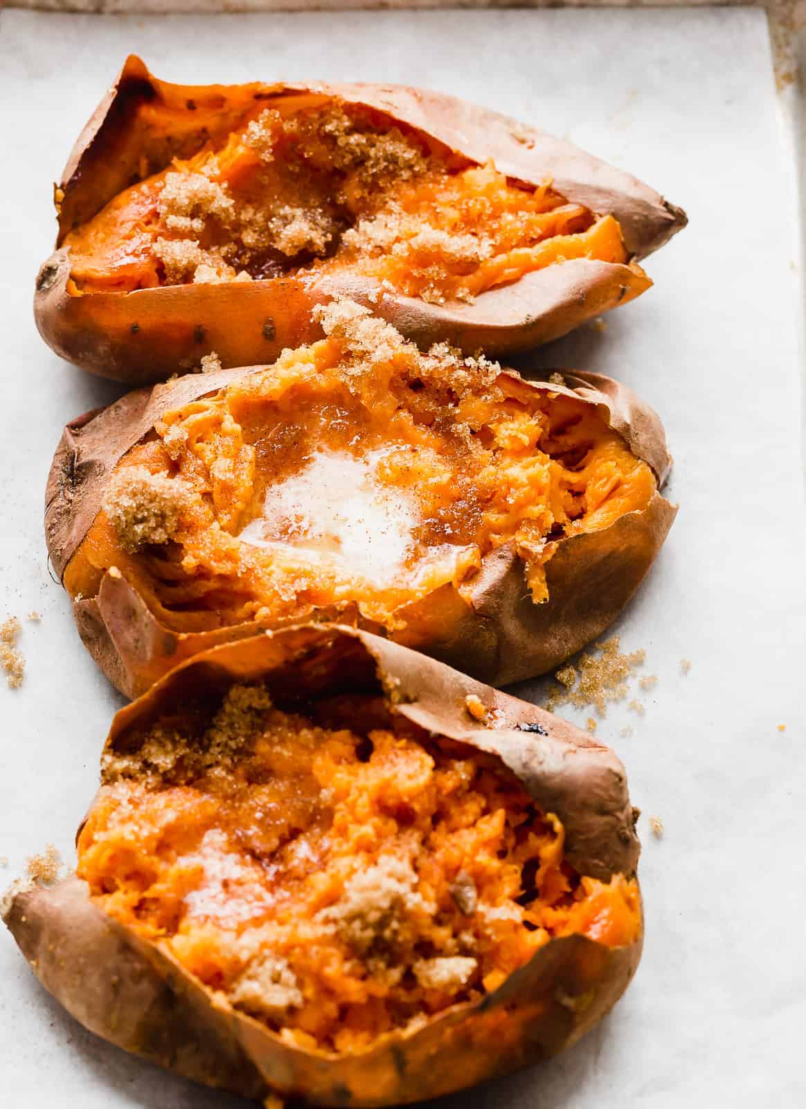 3 Baked sweet potatoes cut open with butter and brown sugar topping.