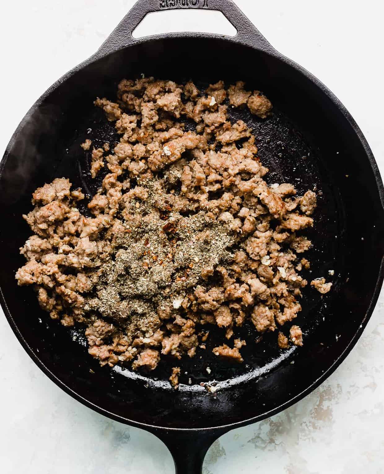A black skillet with cooked Italian sausage with dried herbs sprinkled overtop.