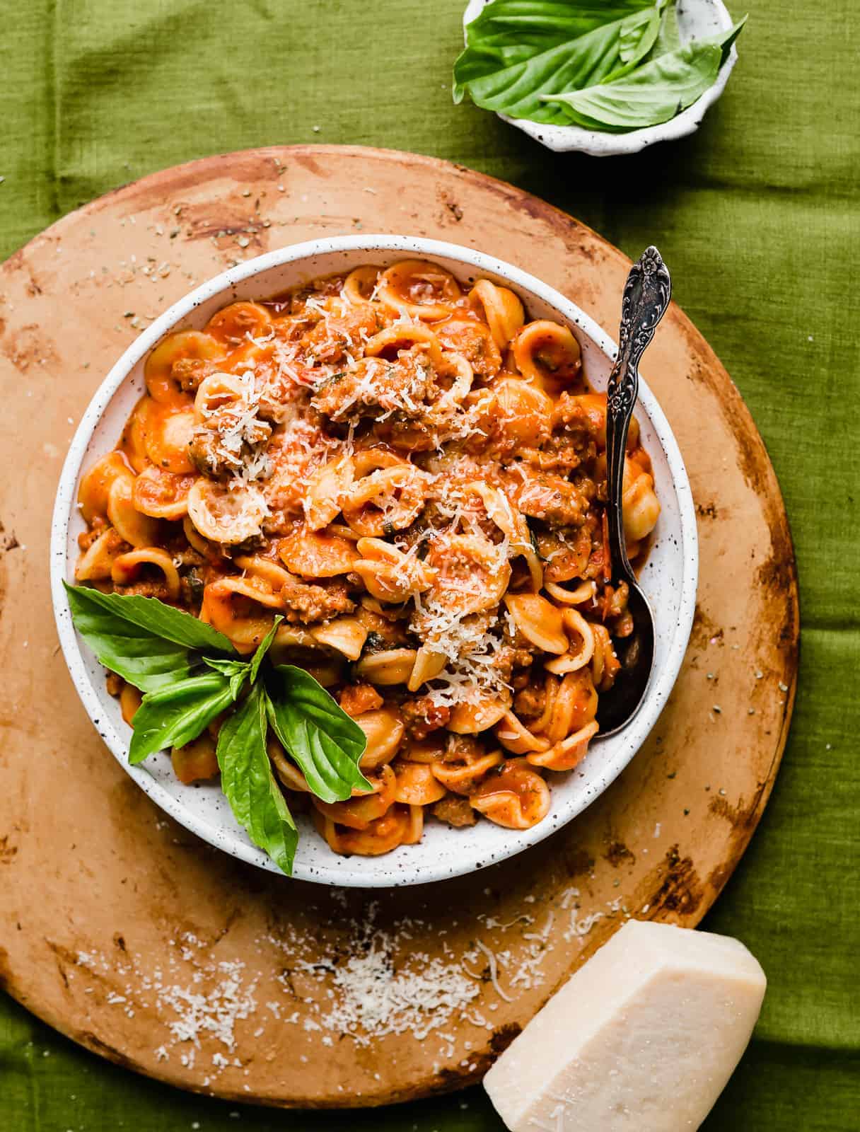 A bowl of bolognese with a garnish of fresh basil, on top of a green linen tablecloth.