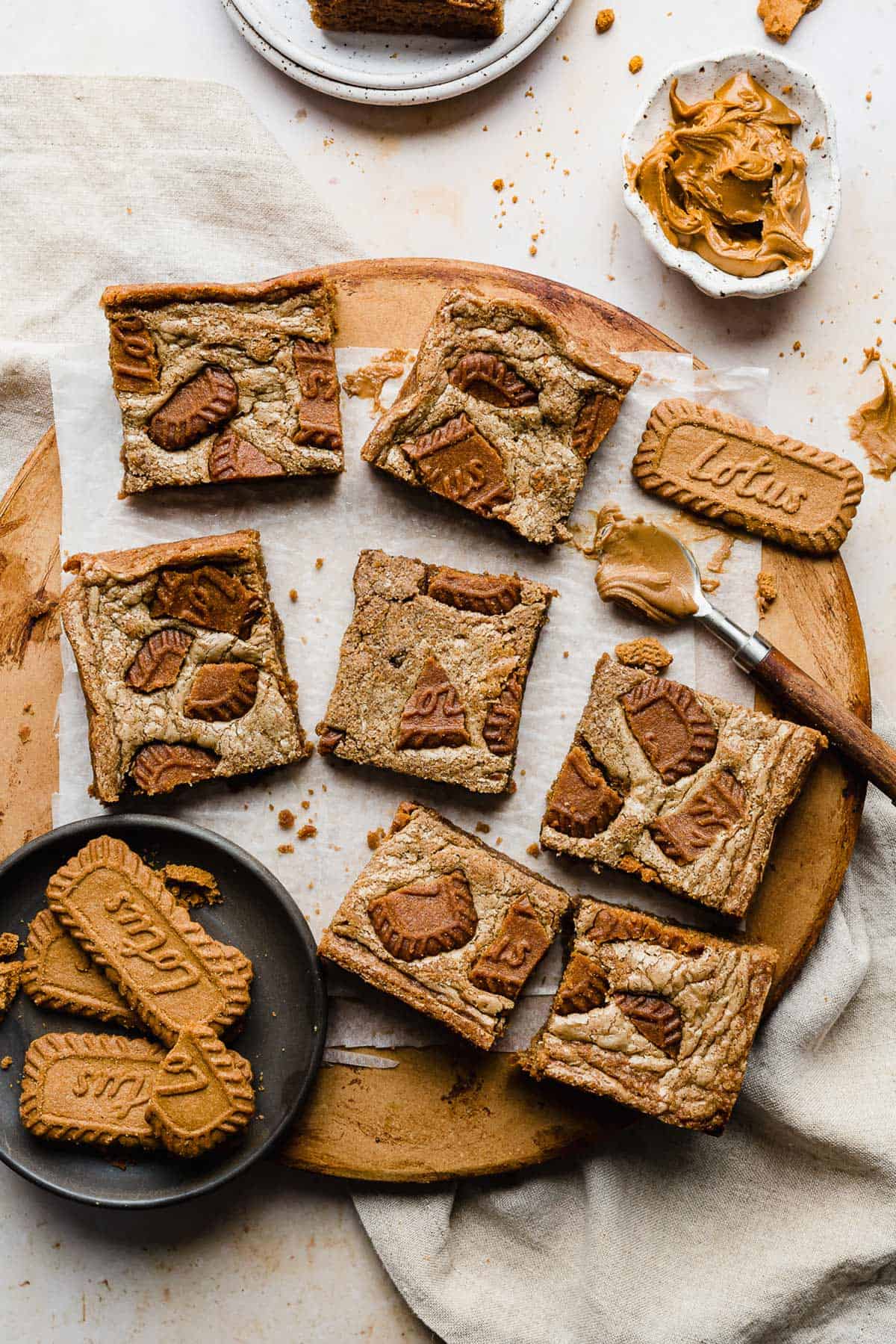 Biscoff Brownies cut into squares resting on a white parchment paper that's on a brown round board.