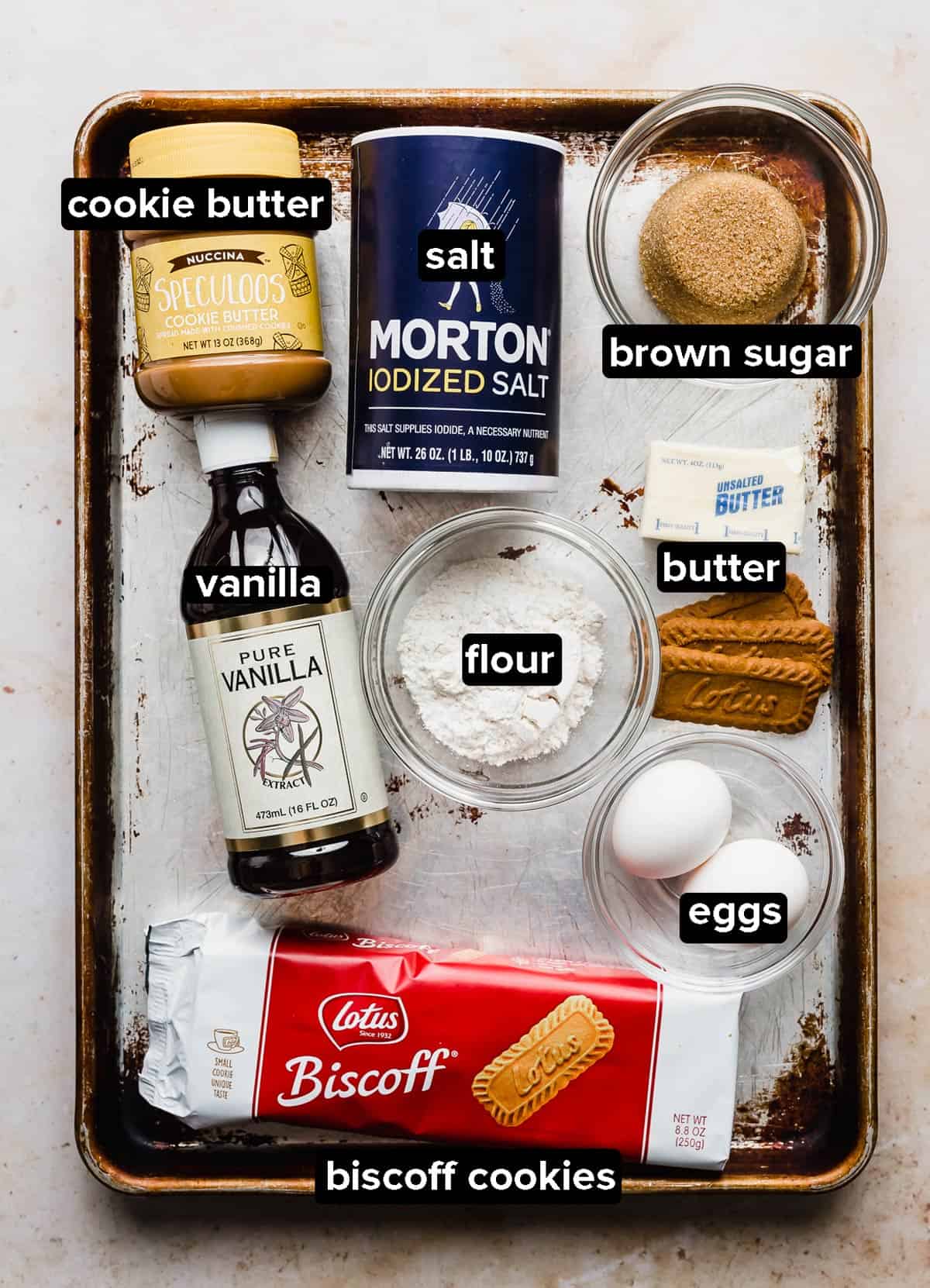 Biscoff Brownies ingredients placed on a worn baking sheet on a white background.