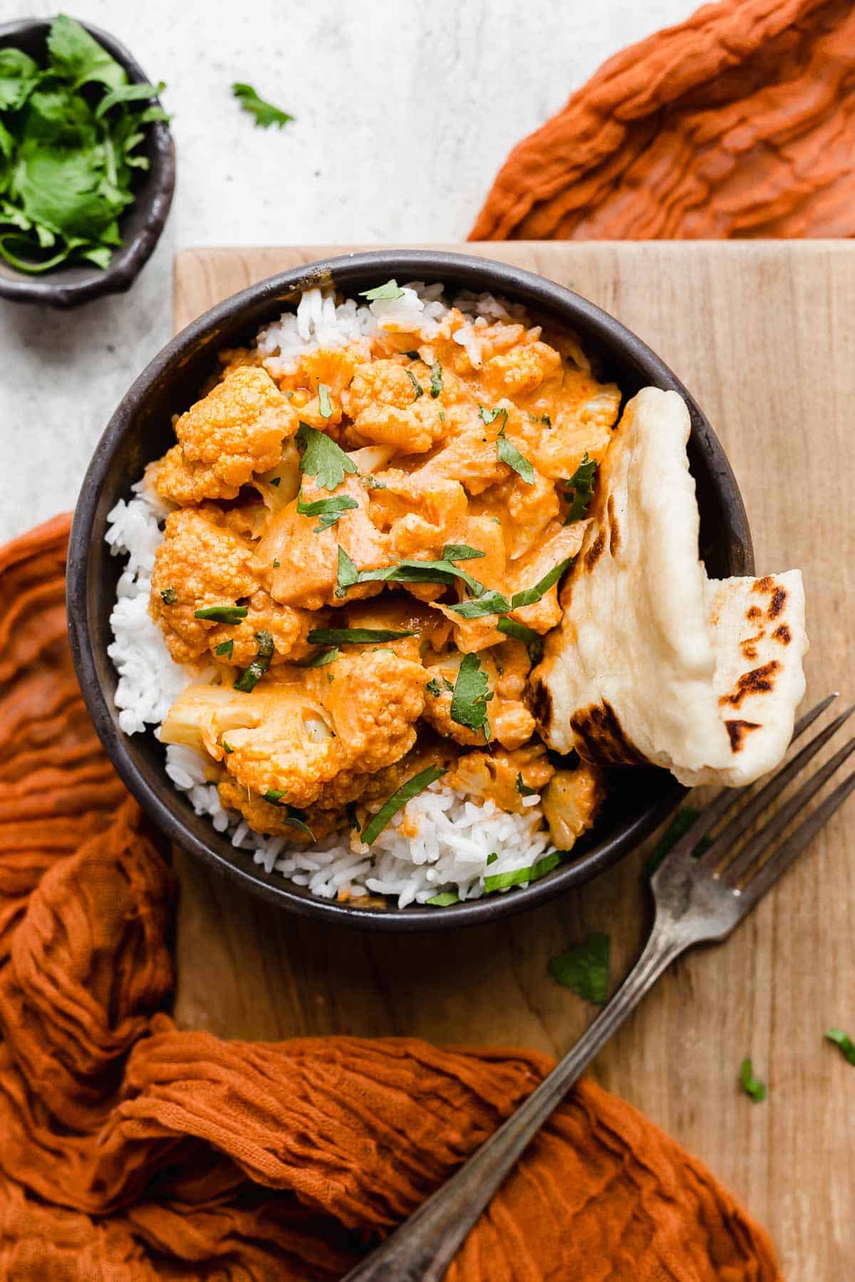 Overhead photo of Indian Butter Cauliflower overtop a bed of white rice in a black bowl and garnished with fresh cilantro.