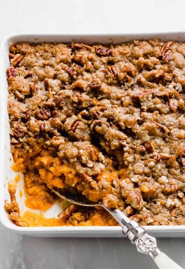 A large serving spoon scooping into a dish of sweet potato casserole. 
