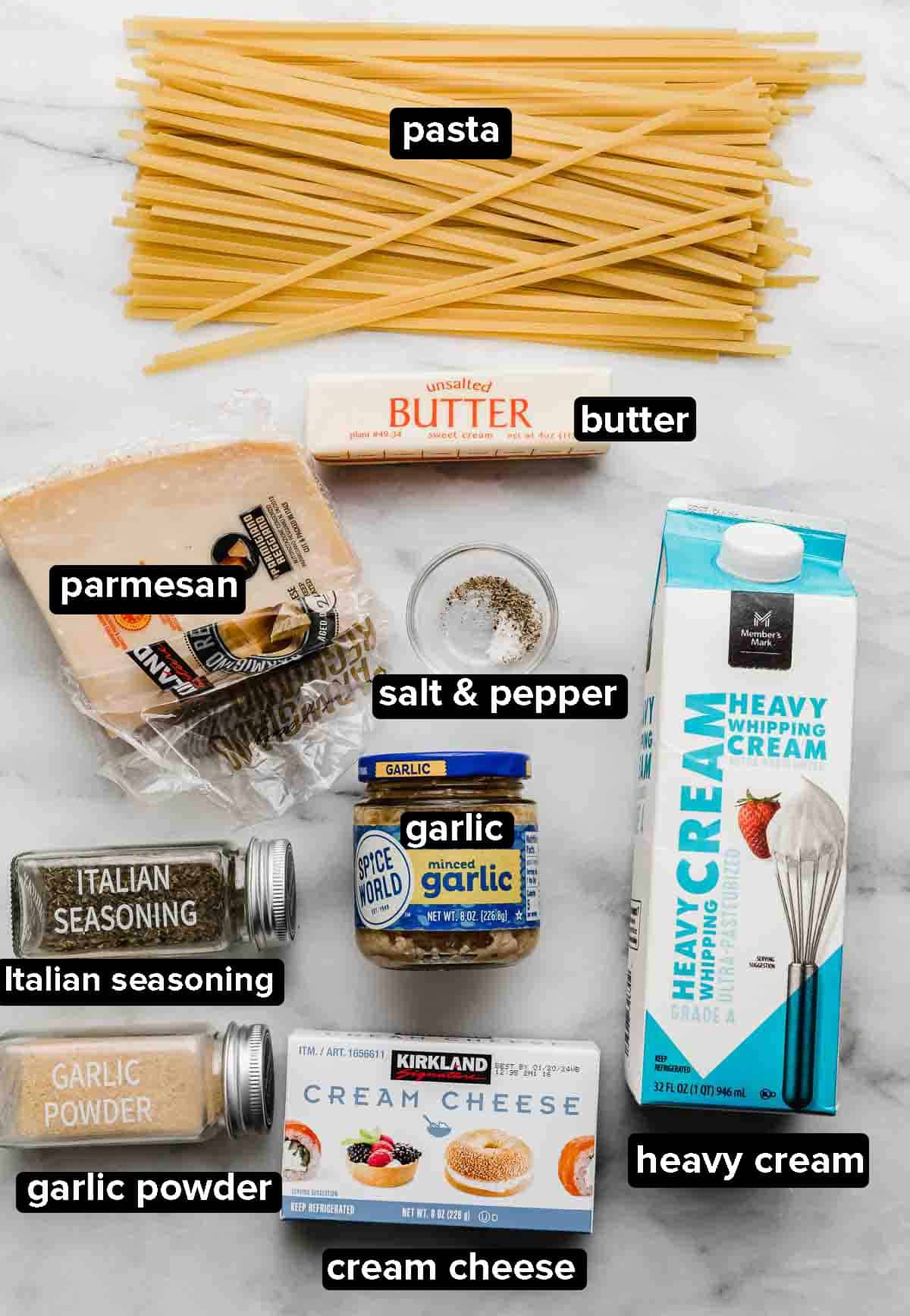 Fettuccine Alfredo ingredients on a white background: heavy cream, cream cheese, parmesan, pasta, salt and pepper, garlic, and Italian seasoning.