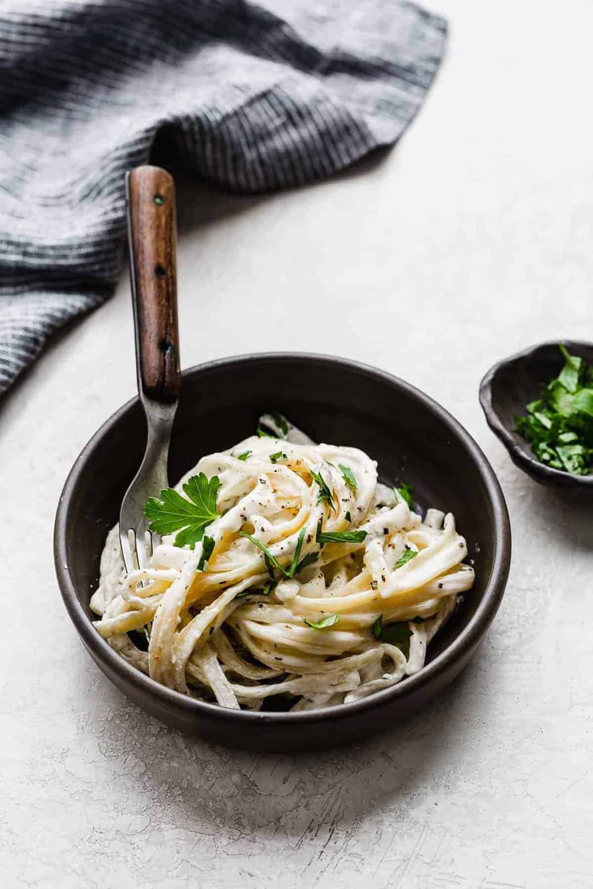 Fettuccine Alfredo in a black bowl on a gray background.