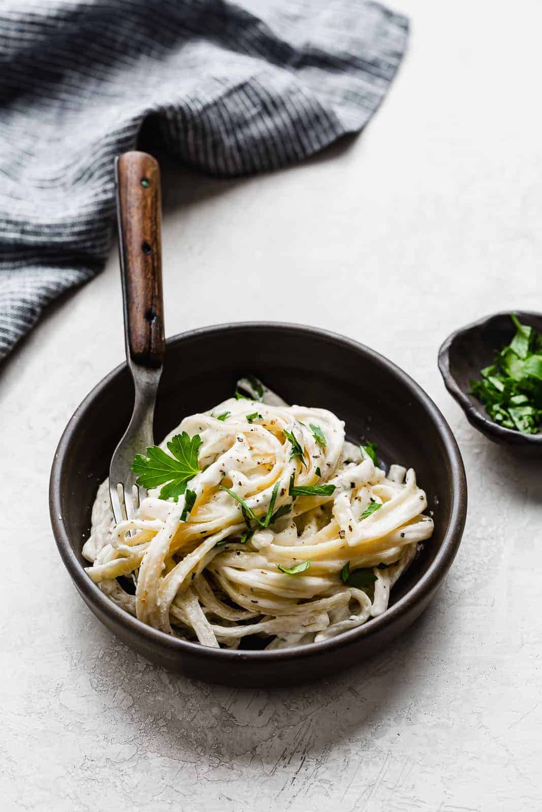 A brown bowl with Fettuccine Alfredo topped with fresh parsley.