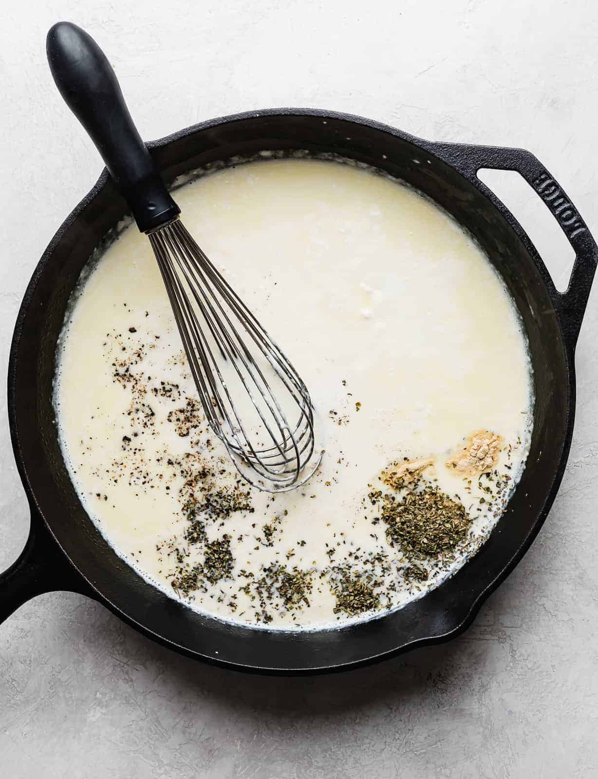 A skillet with cream and seasonings to make Fettuccine Alfredo.