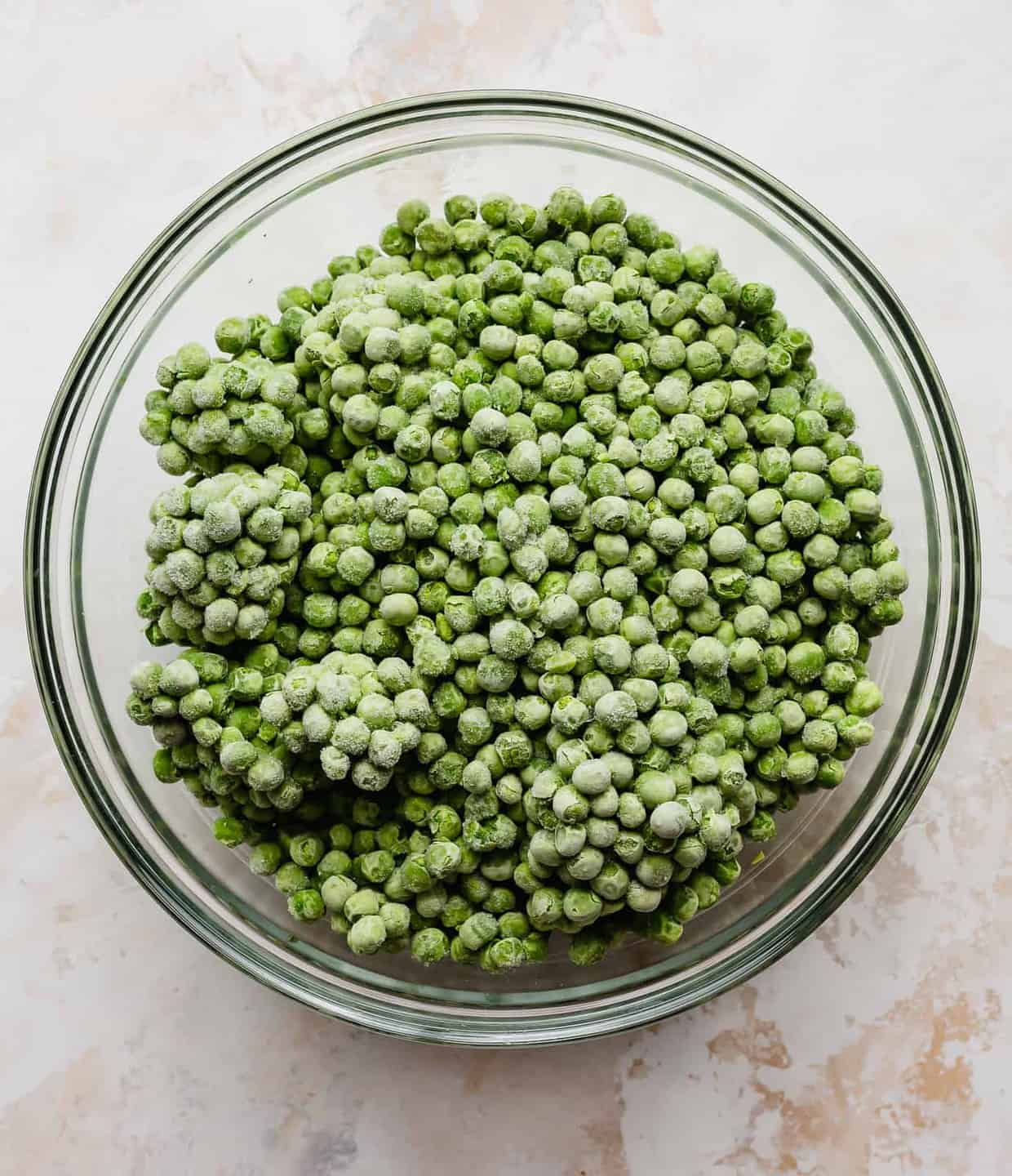 A glass bowl full of frozen peas.