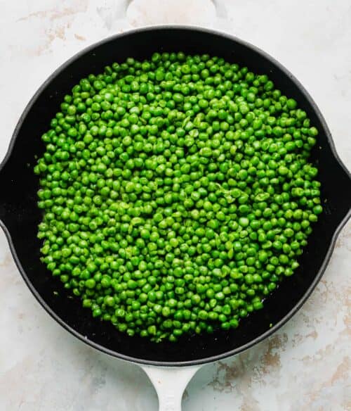 A skillet full of perfectly cooked green peas.
