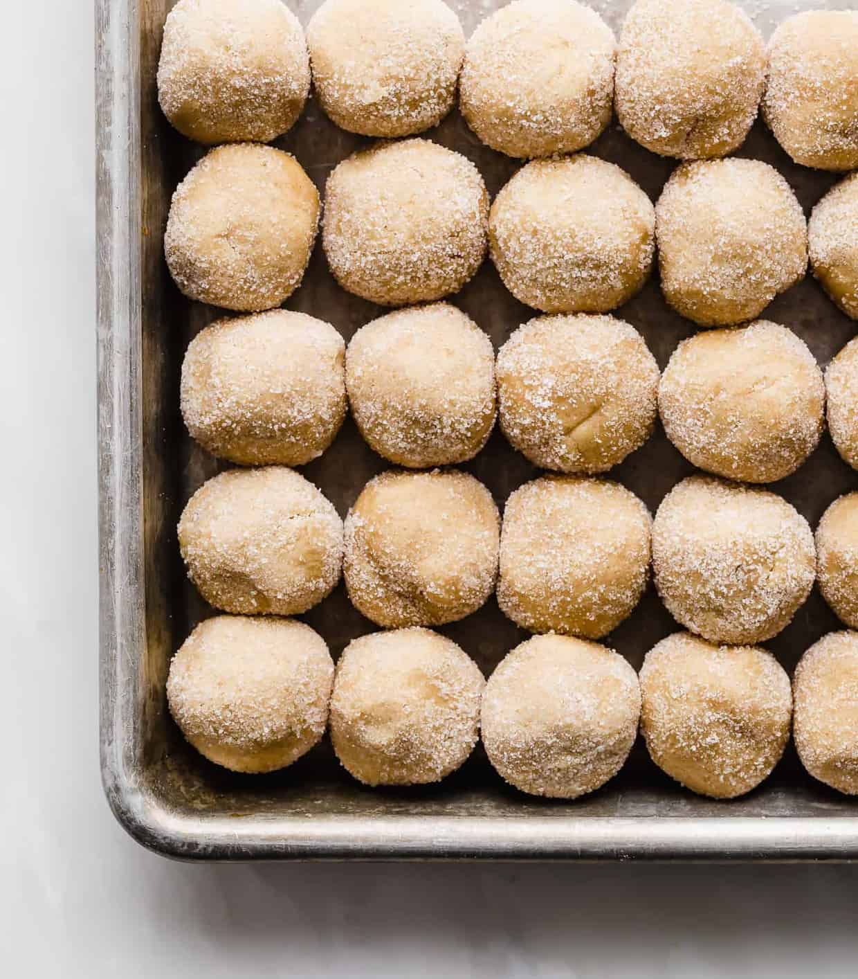 Peanut Butter Blossoms dough balls rolled in granulated sugar, lined up on a cookie sheet.