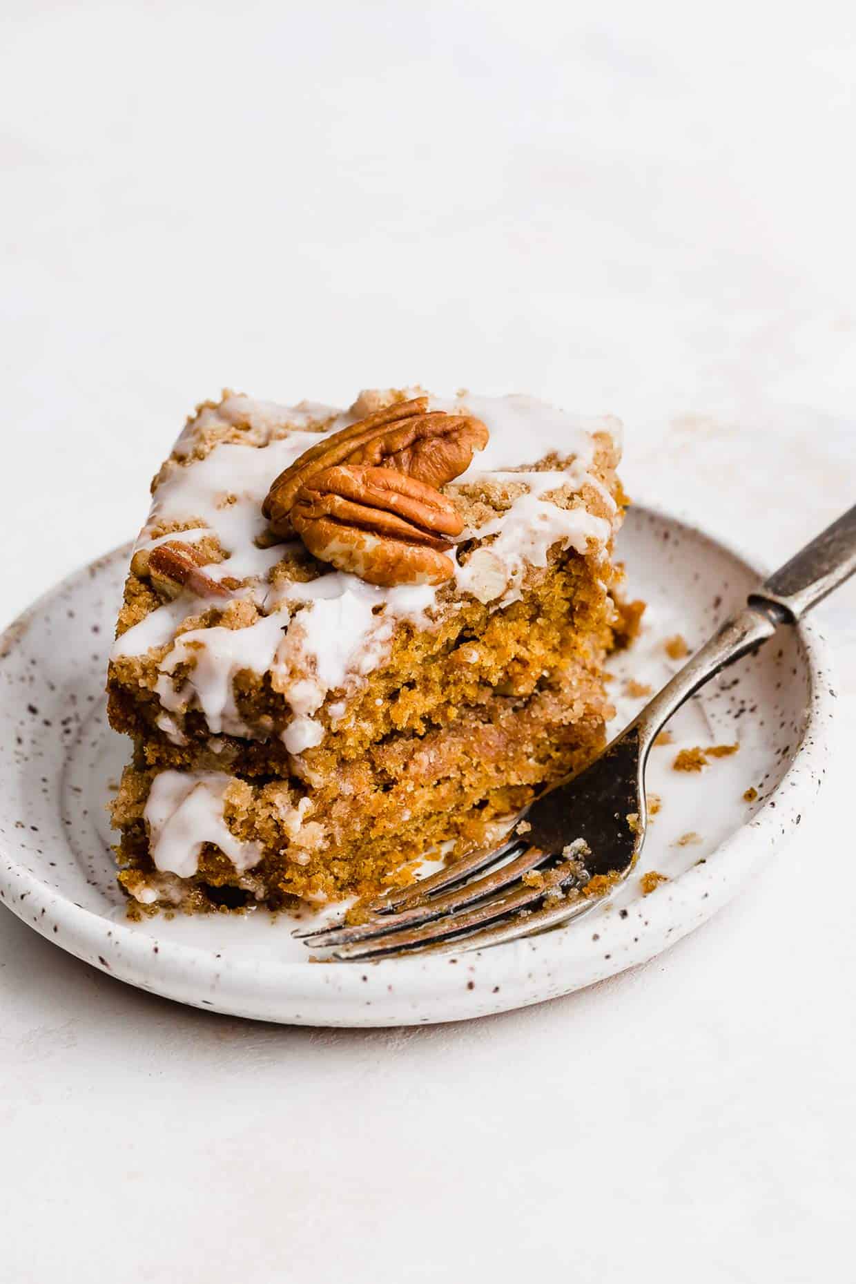 Two pieces of Glazed Pumpkin Coffee Cake stacked on top of each other, on a white plate.