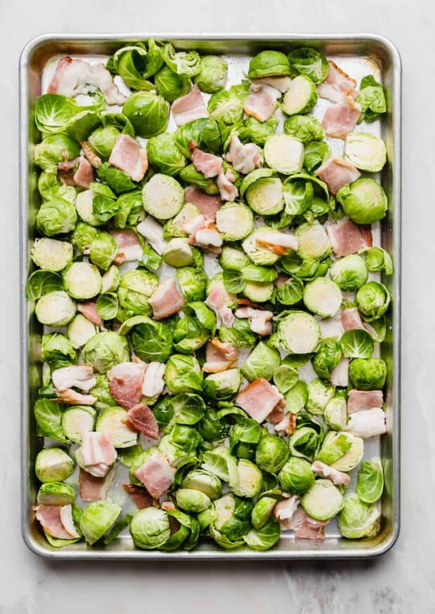A baking sheet full of raw Brussels sprouts and chopped bacon.