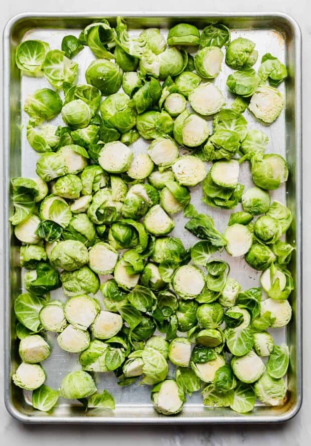 Trimmed and halved Brussels sprouts spread out on a baking sheet.