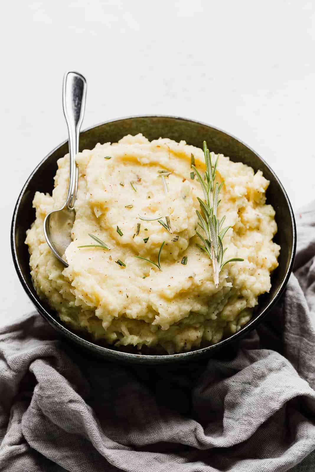 A bowl of mashed potatoes garnished with fresh rosemary.
