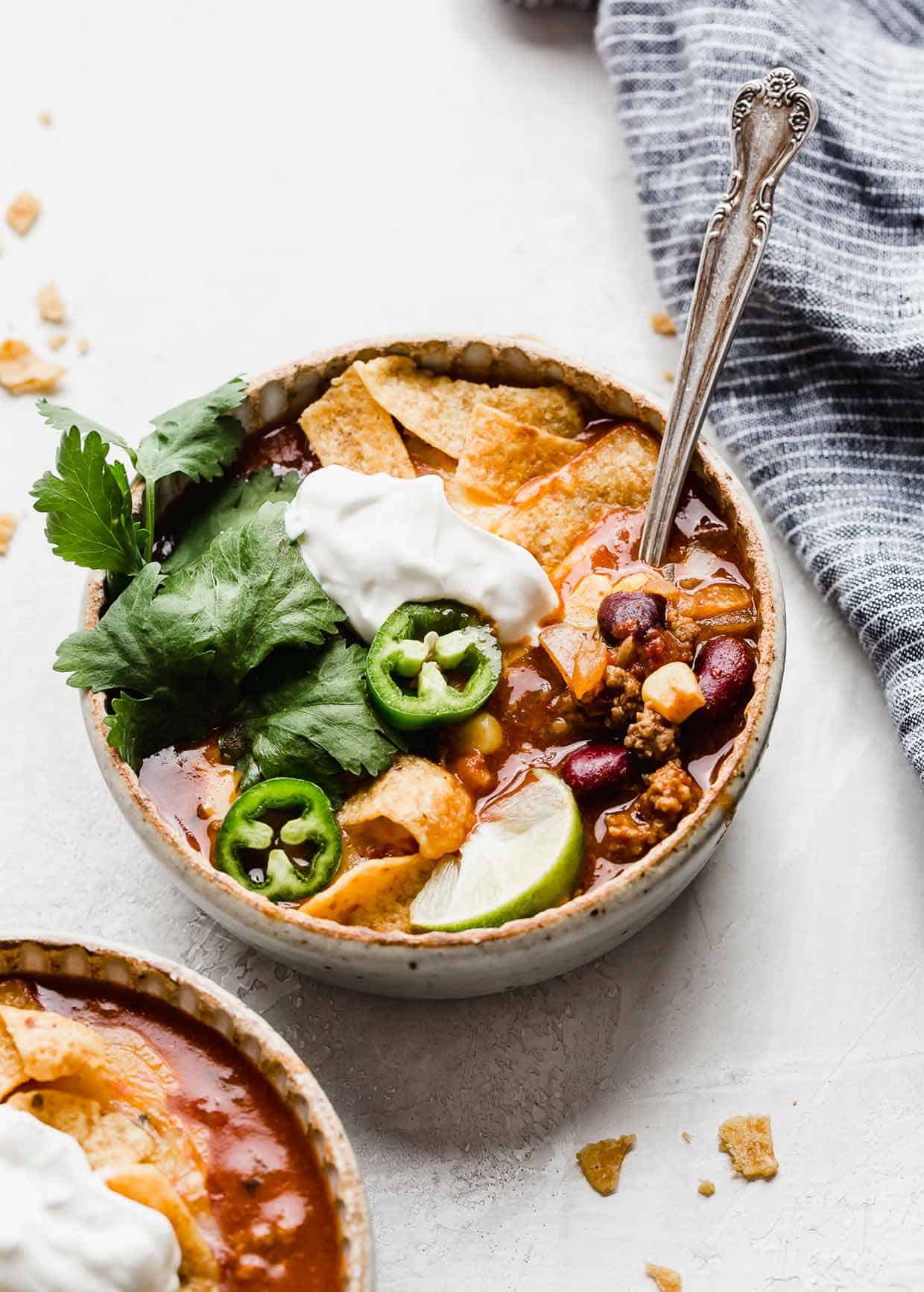 A bowl of Taco Soup with Fritos and sour cream, cilantro, and sliced jalapeños.