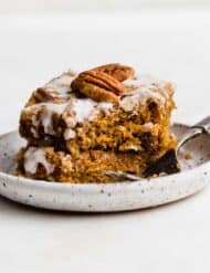 Glazed Pumpkin Coffee Cake topped with a pecan half, on a white plate against a white background.
