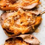 A close up of a Baked Sweet Potato topped with butter and brown sugar with a fork mixing the potato flesh.