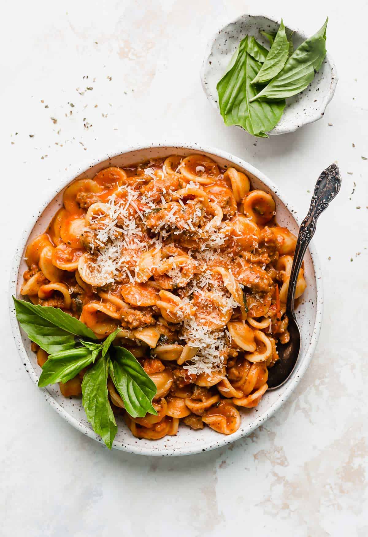 Bolognese recipe in a white pasta plate topped with parmesan on a white background.