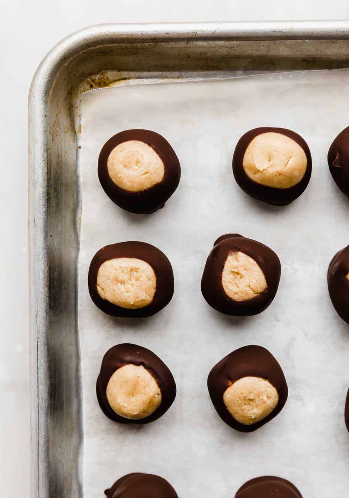 Chocolate dipped buckeyes lined up on a parchment lined baking sheet.