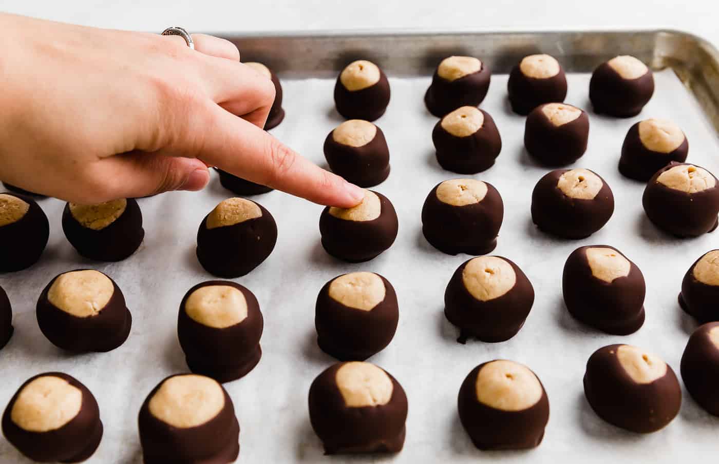 A finger touching a chocolate dipped buckeye.