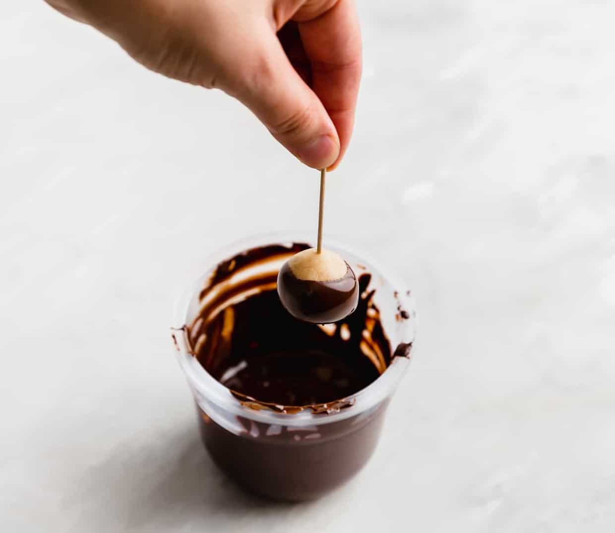 A hand dipping a buckeye into melted chocolate.