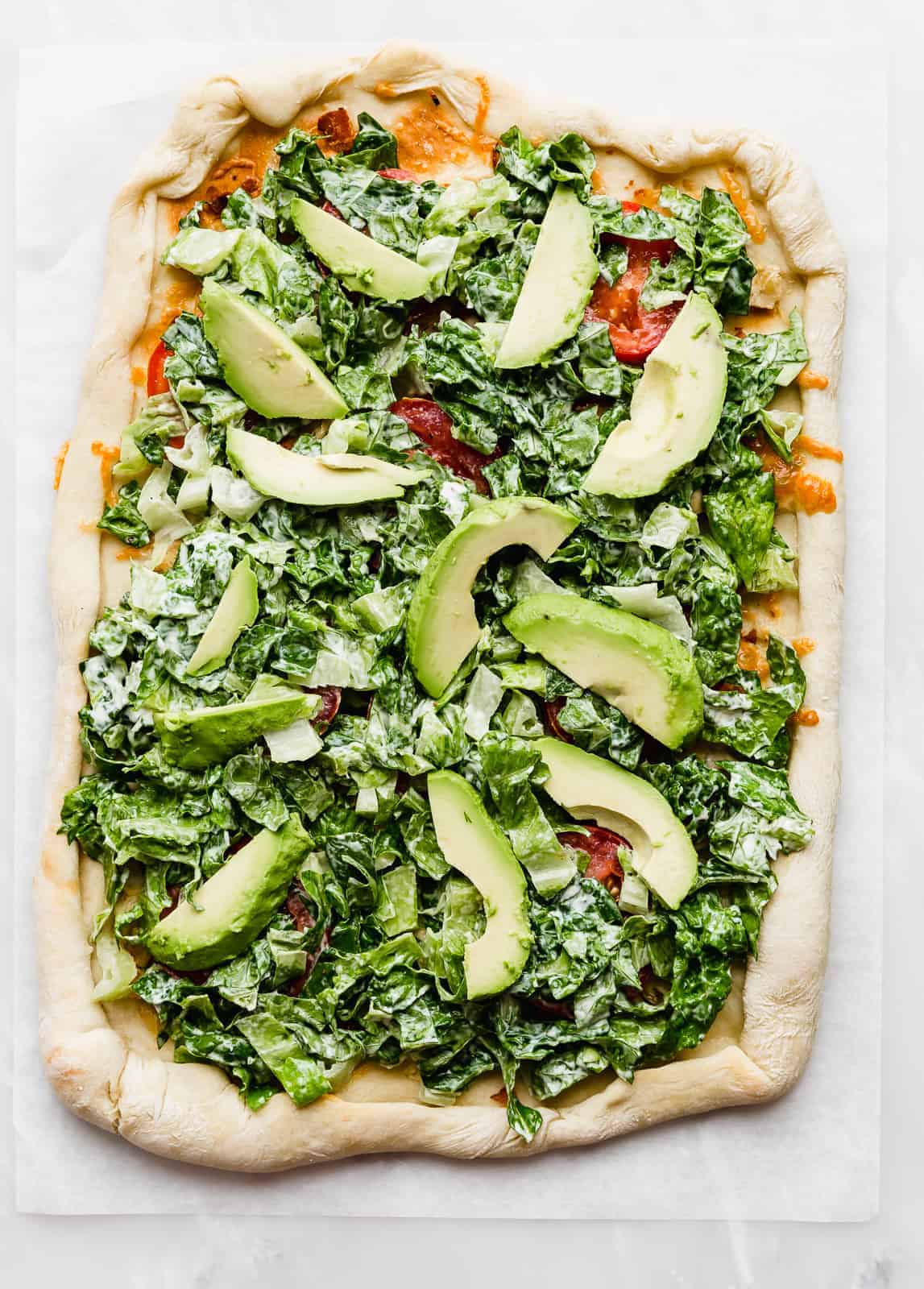 A square pizza topped with lettuce and avocado.