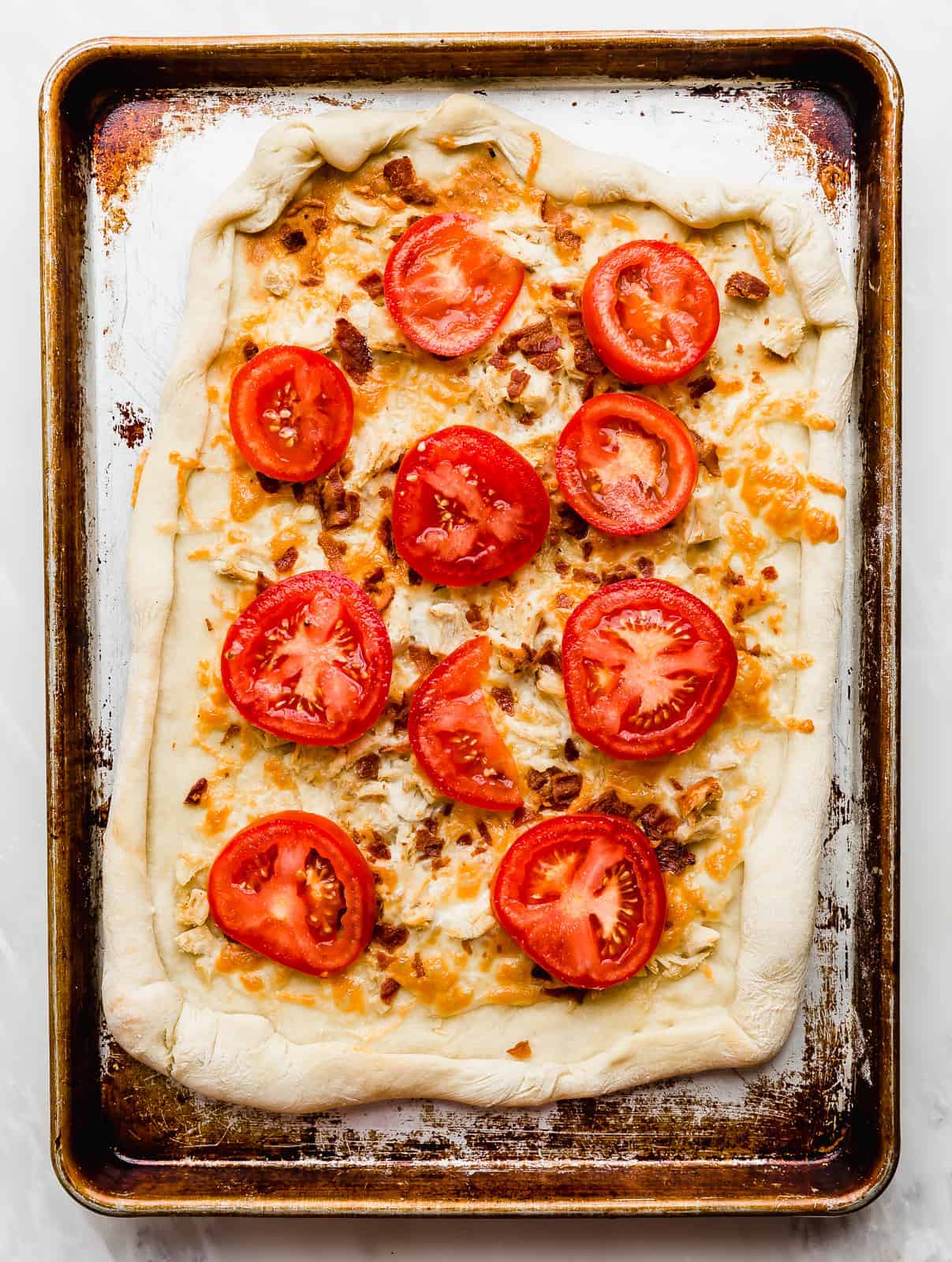 Tomato slices on top of a rectangular baked pizza dough. 