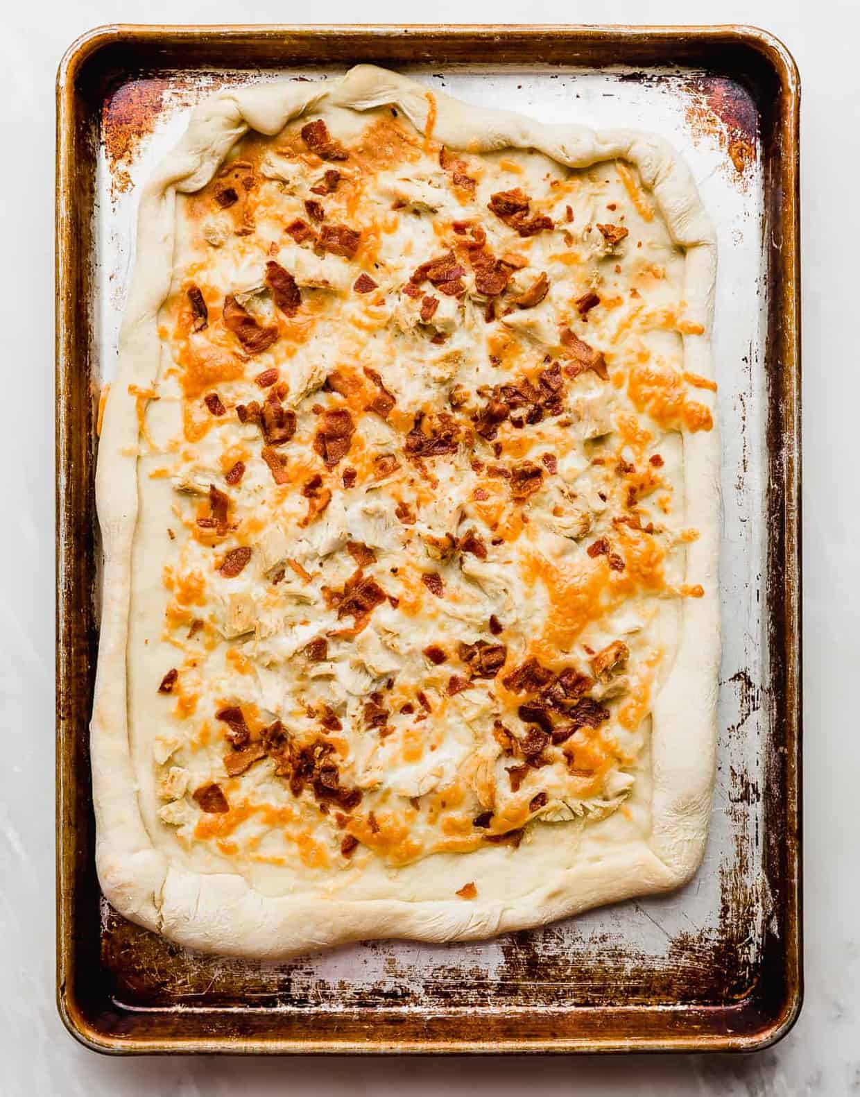 Baked pizza dough topped with cheese, bacon, and chicken.