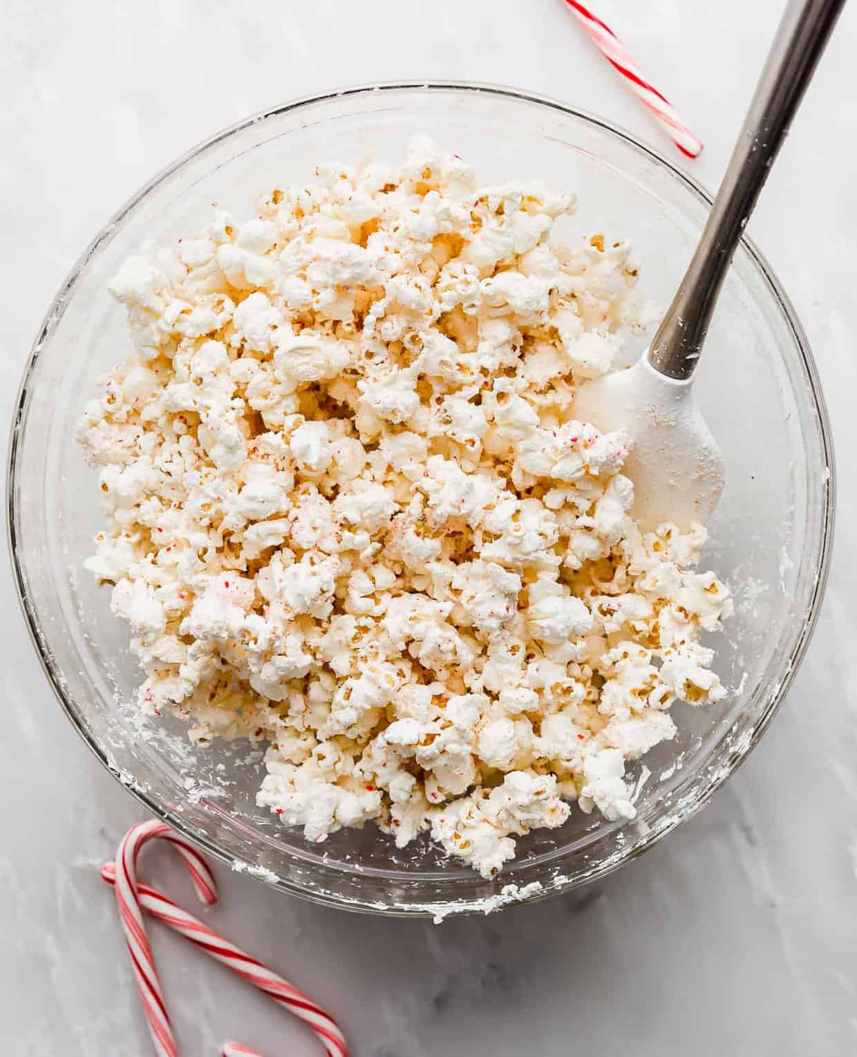 A large glass bowl full of popped popcorn covered in white chocolate and crushed candy canes.