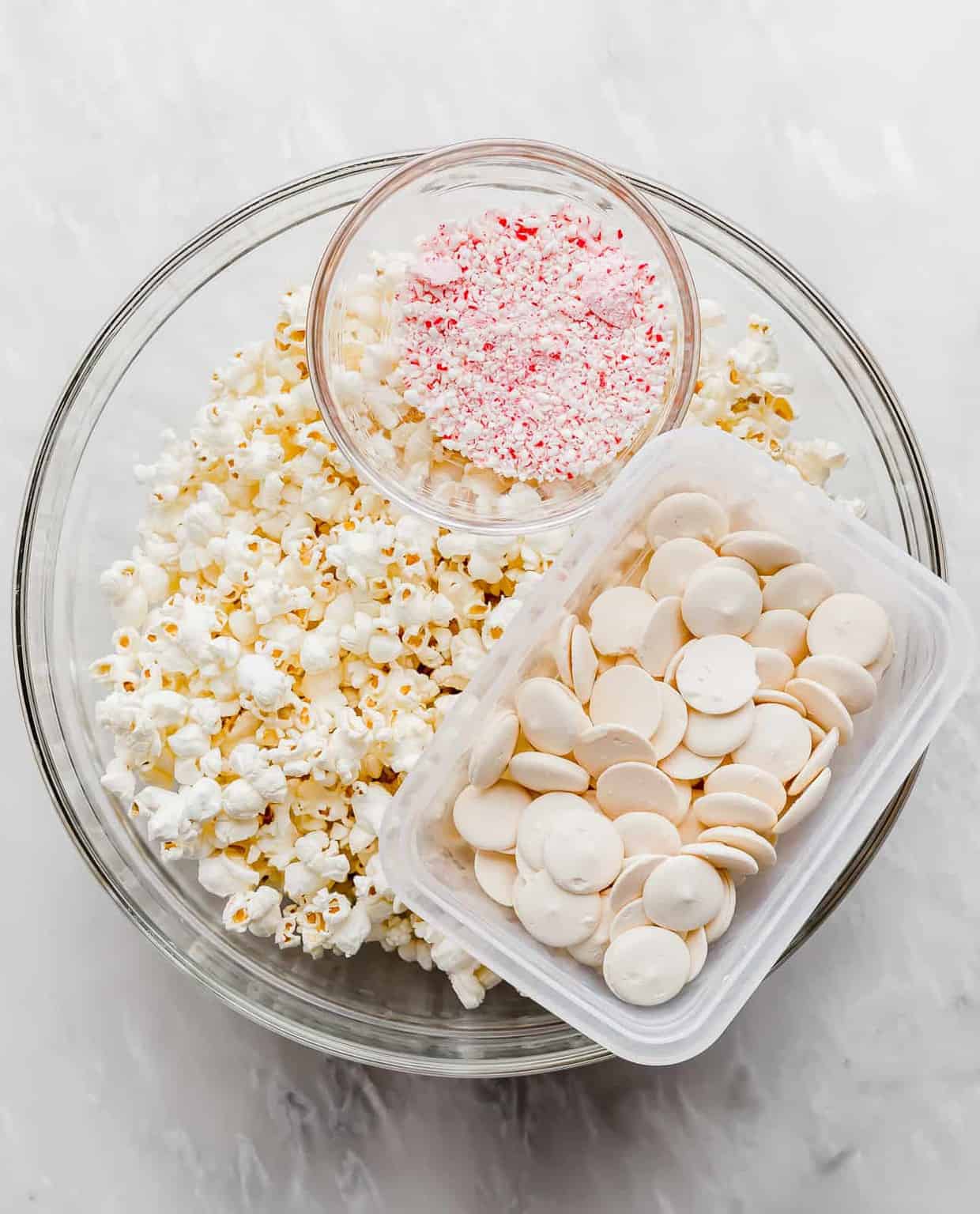 A large bowl of popcorn, a bowl of white candy melts, and a bowl of crushed candy canes.