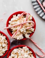 Candy Cane Popcorn in a red bowl with two candy canes on top of the popcorn.
