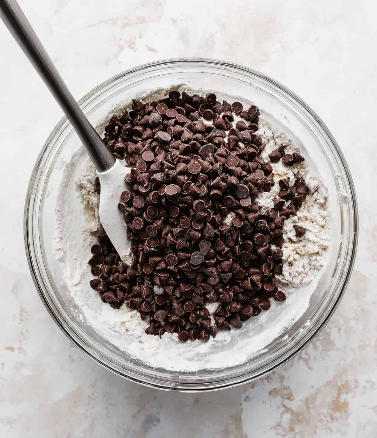 Chocolate chips overtop a mixture of dry ingredients in a glass bowl.