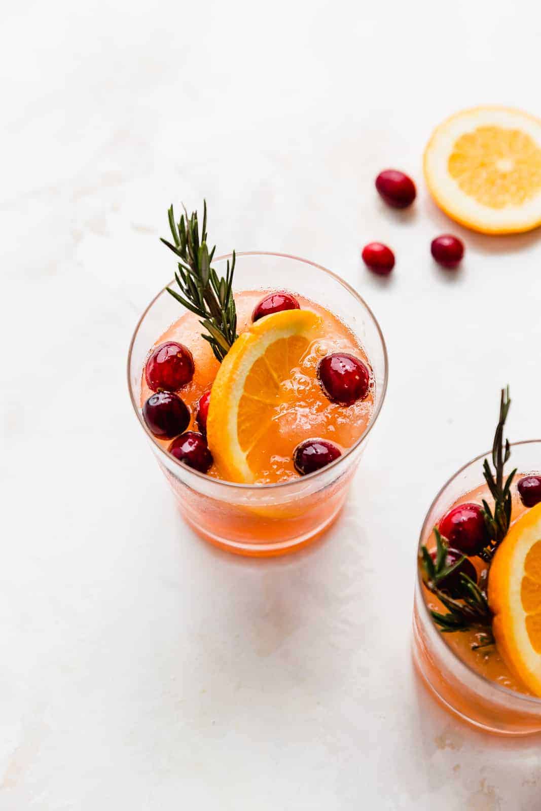 A glass full of slushy Christmas cranberry punch garnished with an orange slice and fresh cranberries.