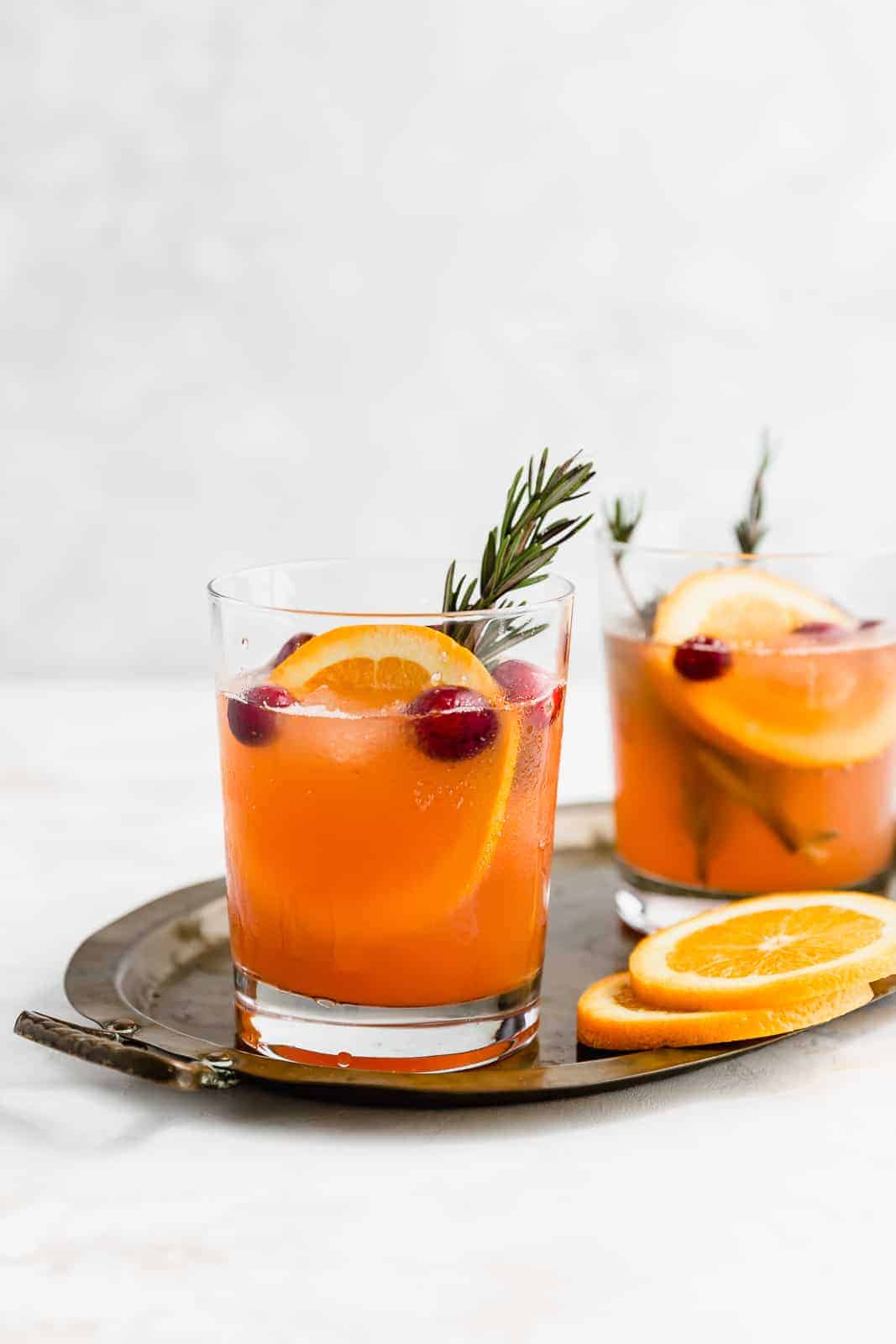 Two glasses of Christmas Slush Punch garnished with rosemary, cranberries, and an orange slice.