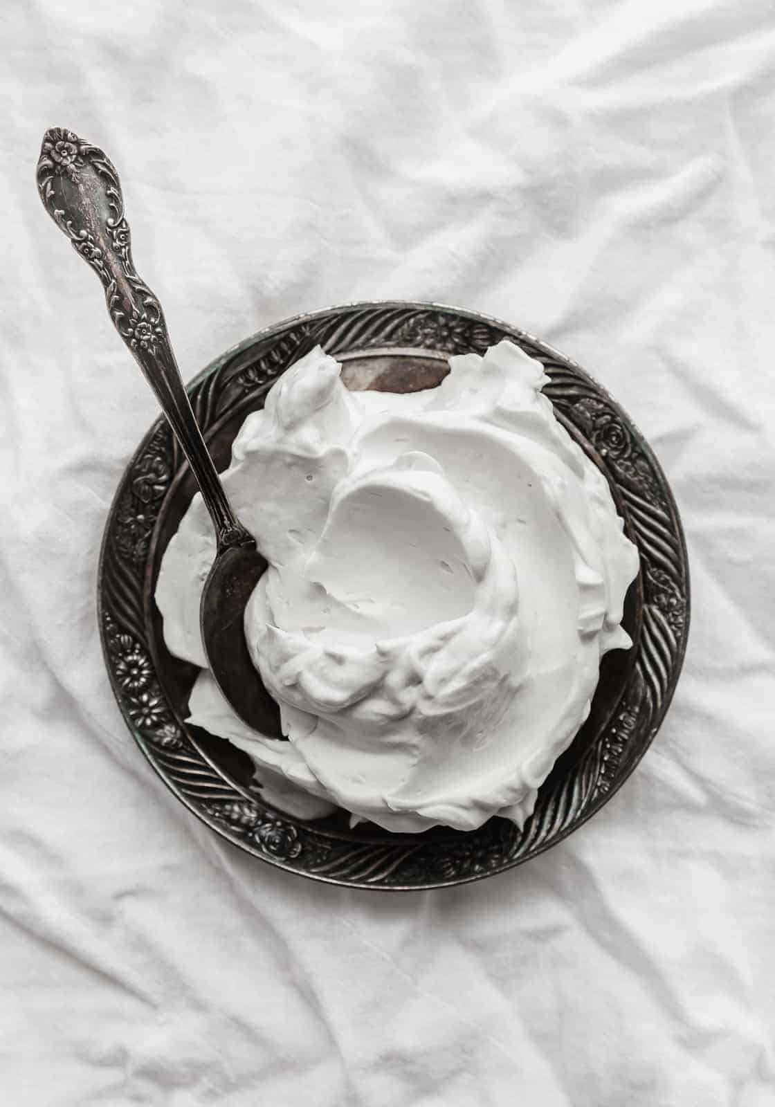 A black plate with coconut whipped cream on it, against a white linen background.